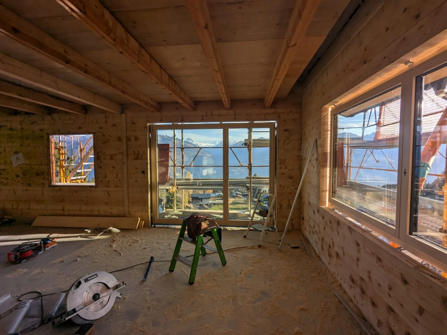 Intérieur en bois massif en cours de construction, grandes baies ouvertes sur les Alpes